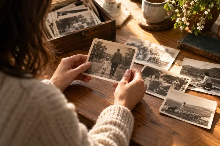 Kleine Sammlung gealterter Familienfotos, die auf einer hellen Holztischplatte betrachtet werden.